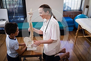 Side view of smiling female therapist explaining boy with artificial spine