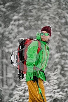 Side view of smiling male skier in goggles and and windproof clothes with ski poles in his hand