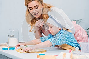 Side view of smiling mother and son rolling dough by rolling