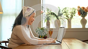 Side view of smiling senior woman flower shop owner taking orders from client on laptop. Small business concept