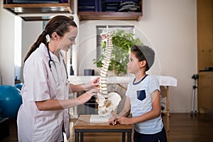 Side view of smiling young female therapist explaining to boy with artificial spine