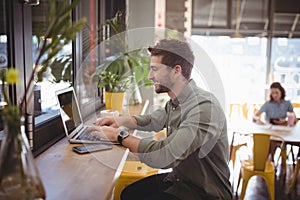 Side view of smiling young man typing on laptop at coffee shop