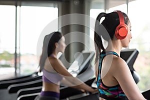 Side View Of Smiling Young Woman Wearing Red Headphones While Exercising On Treadmill In Gym