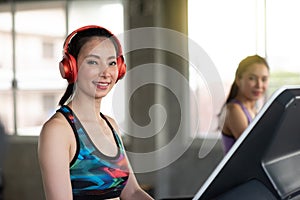 Side View Of Smiling Young Woman Wearing Red Headphones While Exercising On Treadmill In Gym