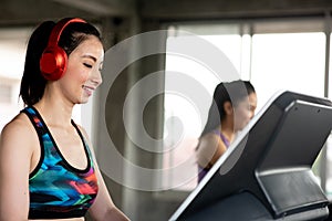 Side View Of Smiling Young Woman Wearing Red Headphones While Exercising On Treadmill In Gym