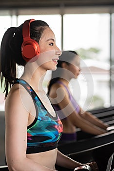 Side View Of Smiling Young Woman Wearing Red Headphones While Exercising On Treadmill In Gym