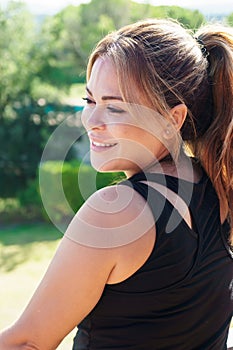 Side view of a Spanish young woman with pony tail smiling and looking away with nature background. Vertical.