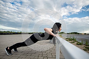 Side view of sports woman doing push ups on horizontal bar outdoors. Woman training near the stadium