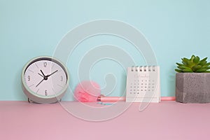 Side view on a still life. Pink fluffy pen, clock and calendar on a pink table