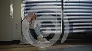 Side view of stressed upset female doctor feeling worried about professional malpractice sitting on floor near window in