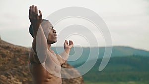 Side view of strong african american bodybuilder stretching outdoor. Mountain landscape background