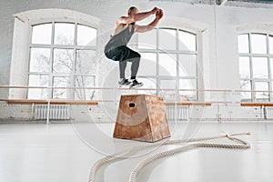 Side view of strong man doing a box jump exercise at workout gym