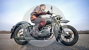 Side view of a stylish cool man in leather jacket driving vintage motorcycle