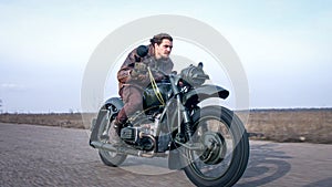 Side view of a stylish cool man in leather jacket driving vintage motorcycle