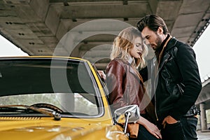 side view of stylish young couple hugging near yellow retro car under