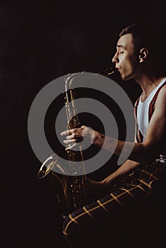 side view of stylish young saxophonist sitting and playing sax