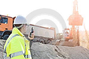 Side view of supervisor using walkie-talkie at construction site against clear sky