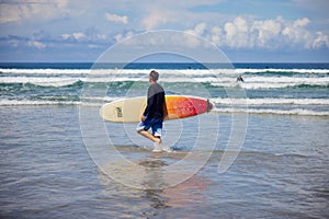 Side view of surfer holding surfboard and walking in water