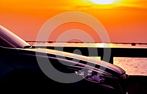 Side view of SUV car with sport and modern design parked on concrete road by sea beach at sunset. Hybrid and electric car