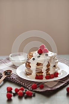 Side view of tasty pancakes in stack with sour cream and resh berries on white plate, muffins decorated with raspberries and