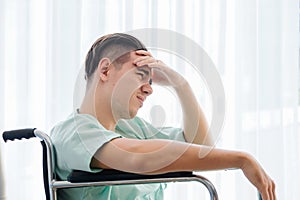 Side view, Teenage caucasian Male patient having stressed pose hand on head and sitting on wheelchair in hospital room.