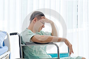 Side view, Teenage Male patient having stressed pose hand on head and sitting on wheelchair in hospital room