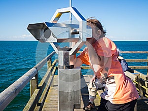 Boy is looking through a binocular at the sea