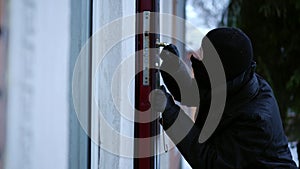 Side view thief picking lock entering empty house on winter day. Caucasian young man in ski mask breaking in private