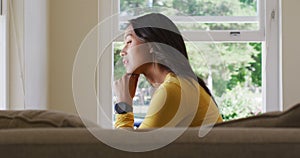 Side view of thoughtful biracial woman sitting and looking outside window