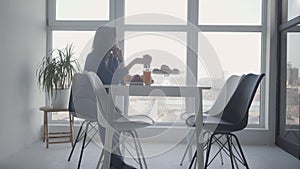 Side view of thoughtful caucasian woman holding apple and looking out the window. Wide shot of sad brunette lady sitting