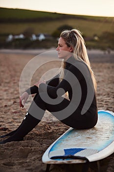 Side View Of Thoughtful Woman Wearing Wetsuit On Surfing Staycation Looking Out To  Sea At Waves