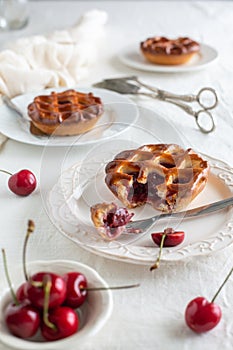 Side view of three individual cherry pies white plates with one pie cut open with a fork  white background and cherries around