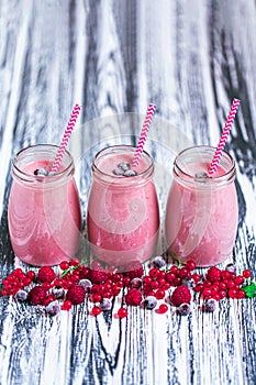 Side view of three jars with yogurt smoothie with cranberry, raspberry, blueberry on wooden table