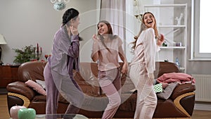 Side view three joyful female friends having fun dancing simultaneously in pajamas in living room. Happy carefree