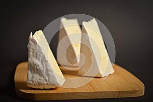 Side view of three pieces Soft French Brie cheese cuts served on wooden board