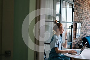 Side view of tired redhead young woman yawning while working on laptop computer sitting at table