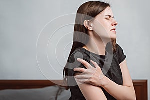 Side view of tired unhappy young woman sitting on bed at home massaging shoulder, upset girl suffer from discomfort muscle pain