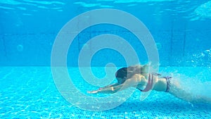 Side view to sexy woman swimming under water at pool. Girl wearing red bikini floating in basin. Female tourist enjoying