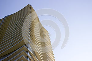 Side view of the top part of a modern corporate building with yellowish overhangs in each floor.