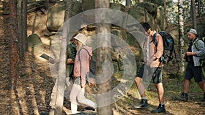 Side view of tourists friends walking in forest on summer day holding map talking