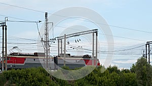 Side view of a twinned red and gray electric locomotive running on a railroad on a fine summer day