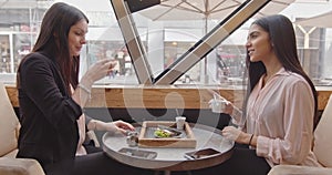 Side view of two adult business women sitting and talking in a bar. Having breakfast in a cafe, two multi-cultural