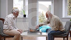 Side view two concentrated old Caucasian men thinking playing chess indoors. Focused male senior friends enjoying game