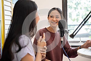 side view of two girls laughing while having a dialogue on a podcast show using a microphone