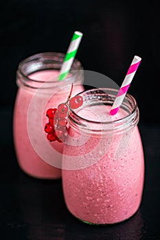 Side view of two jars with yogurt pink smoothie with berries on black background. Selective focus