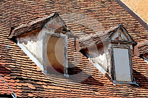 Side view of two old style roof windows closed with wooden boards covered with dilapidated red roof tiles and cracked facade