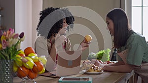 Side view of two positive young women talking holding healthful fruits in hands. Portrait of Asian and African American