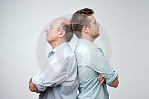 Side view of two serious men father and son standing back to back against a white background