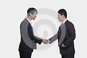 Side view of two smiling businessmen shaking hands, studio shot