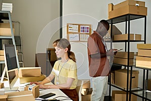 Side view of two young intercultural workers of warehouse checking data